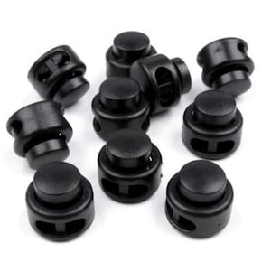 May include: A close-up of ten black plastic toggle clasps. The clasps are designed to be used for securing straps or cords.