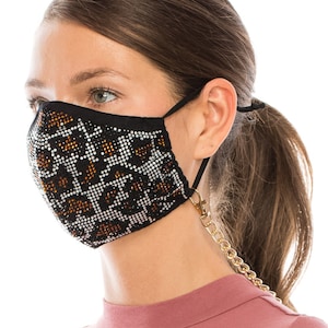 May include: A black face mask with a gold chain attached. The mask has a geometric pattern of rhinestones in silver and brown.