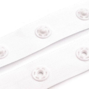 May include: White fabric tape with white plastic snap buttons. The tape is folded in half, showing the buttons on both sides.