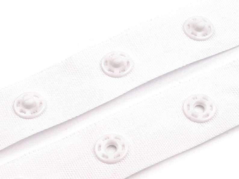 May include: White fabric tape with white plastic snap buttons. The tape is folded in half, showing the buttons on both sides.