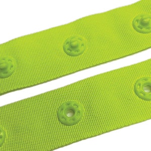 May include: A close-up of lime green fabric with rows of plastic snap buttons. The fabric is textured and the buttons are round with a raised center.