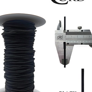 May include: A spool of black elastic cord, wound around a white cardboard spool. The cord is measured with a caliper, showing a diameter of 1/8 inch. The text "BLACK GY10006" is printed below the spool.
