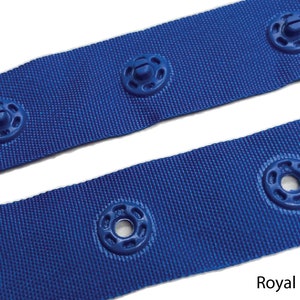May include: Royal blue webbing with plastic snap fasteners. The webbing is 1 inch wide and has a woven texture.