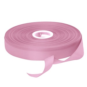 May include: A roll of pink satin ribbon. The ribbon is wound around a spool and a length of ribbon is hanging off the spool.