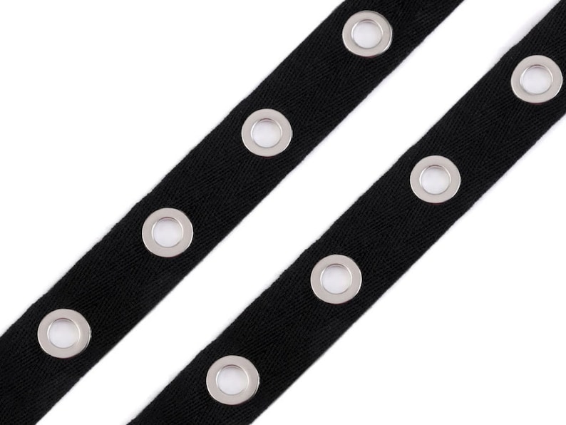 May include: Black cotton ribbon with silver grommets. The ribbon is approximately 1 inch wide and has a herringbone weave.