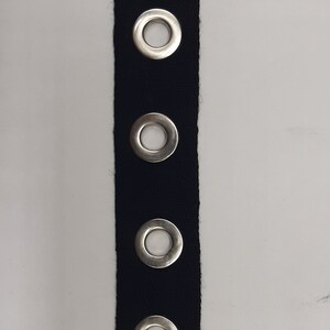 May include: Black fabric trim with silver grommets. The trim has five grommets evenly spaced along the length of the fabric.