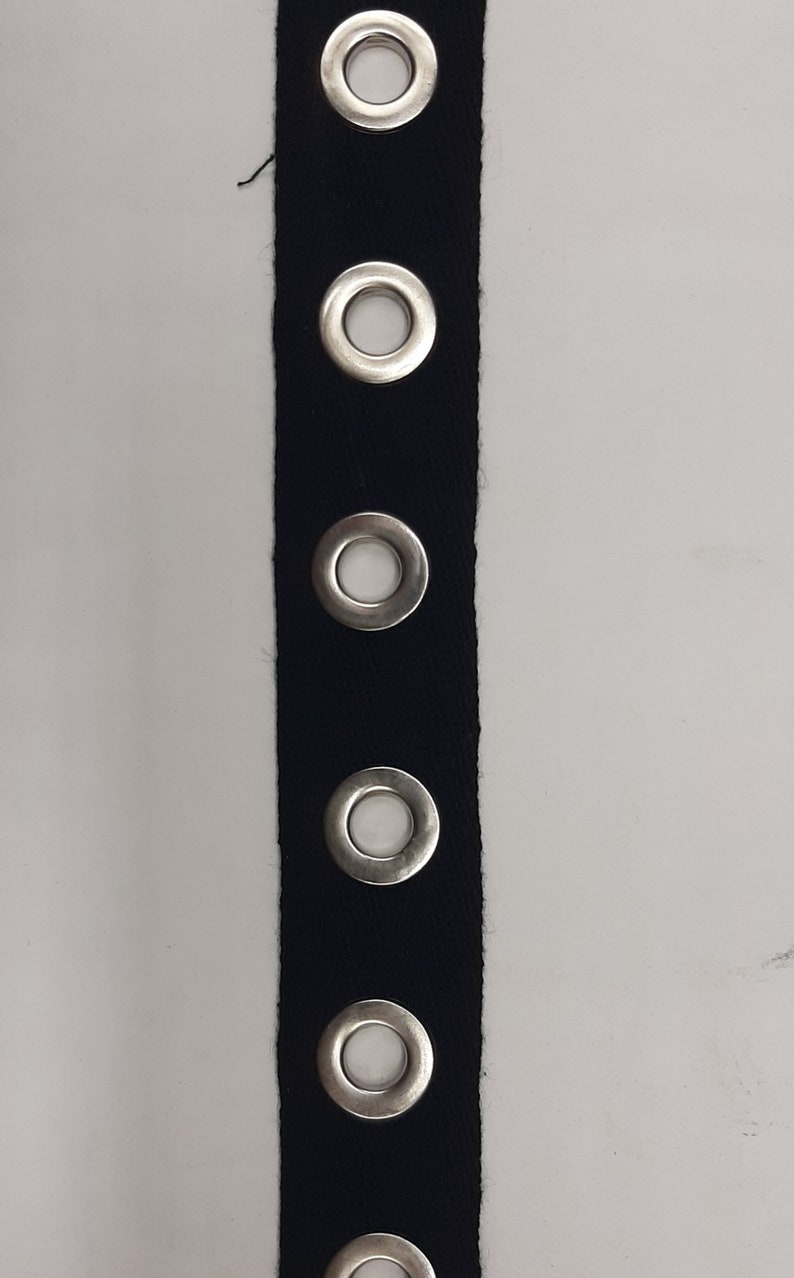 May include: Black fabric trim with silver grommets. The trim has five grommets evenly spaced along the length of the fabric.