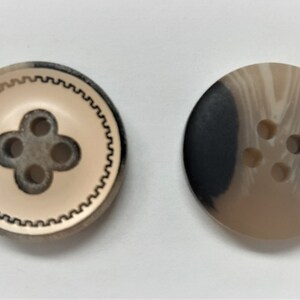 May include: Two round buttons with a four-hole design. One button is beige with a black and white swirl pattern. The other button is beige with a black border and a black four-hole design.