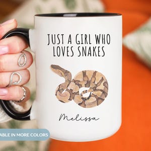 Könnte beinhalten: Weißer Keramikbecher mit schwarzem Innenraum und Henkel. Der Becher zeigt den Text "JUST A GIRL WHO LOVES SNAKES" über einer Aquarellillustration einer Schlange. Der Name "Melissa" steht darunter.