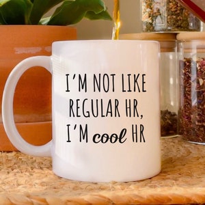 May include: White ceramic mug with black text that reads "I'm not like regular HR, I'm cool HR".