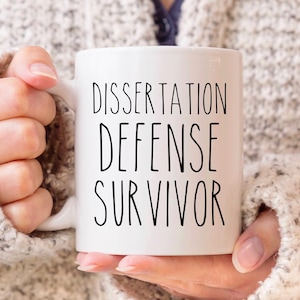 May include: White ceramic mug with black text that reads "Dissertation Defense Survivor".