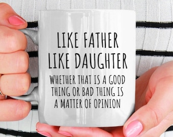 Könnte beinhalten: Eine weiße Keramiktasse mit schwarzem Text, der "Like Father Like Daughter. Whether that is a good thing or bad thing is a matter of opinion." lautet.