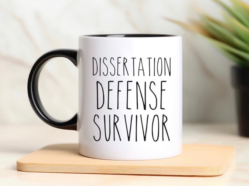 May include: White ceramic coffee mug with a black handle and black rim. The mug has the text "Dissertation Defense Survivor" printed in black.