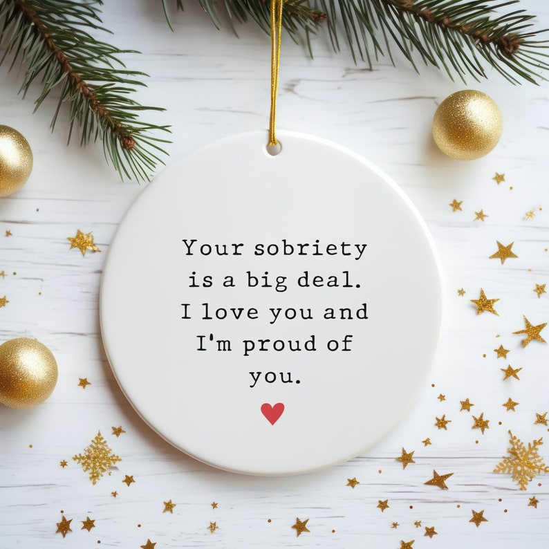 K&ouml;nnte beinhalten: Wei&szlig;er Keramik-Weihnachtsbaumschmuck mit dem Text "Deine N&uuml;chternheit ist eine gro&szlig;e Sache. Ich liebe dich und ich bin stolz auf dich." und einem kleinen roten Herzen.