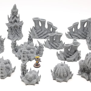Puede incluir: Un conjunto de piezas de terreno grises impresas en 3D para juegos de mesa. El conjunto incluye varias estructuras con diseños orgánicos y alienígenas, como agujas, muros y formaciones esféricas. Se incluye una figura en miniatura para la escala.