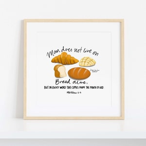 Op de afbeelding: Een ingelijste print met illustraties van verschillende soorten brood, waaronder een croissant en een brood. De tekst luidt: 'De mens leeft niet van brood alleen, maar van elk woord dat uit de mond van God komt. Mattheüs 4:4.'