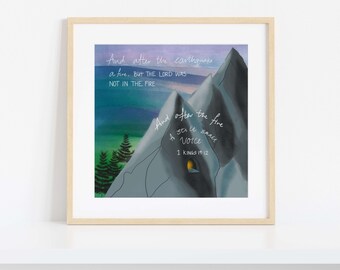 May include: A framed art print with a mountain scene and a quote from 1 Kings 19:12. The image shows a mountain range in grey and blue, with green trees and a sunset sky. The text is in white script.