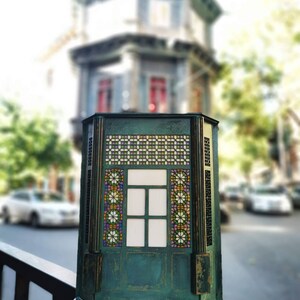 K&ouml;nnte beinhalten: Eine gr&uuml;ne, h&ouml;lzerne Dekorationsbox mit einem Buntglasfenster. Das Fenster hat ein geometrisches Muster mit bunten Glasscheiben. Die Box steht auf einem schwarzen Metallgel&auml;nder.