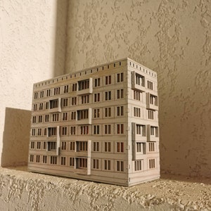 May include: A small, white cardboard model of an apartment building with many windows and balconies.