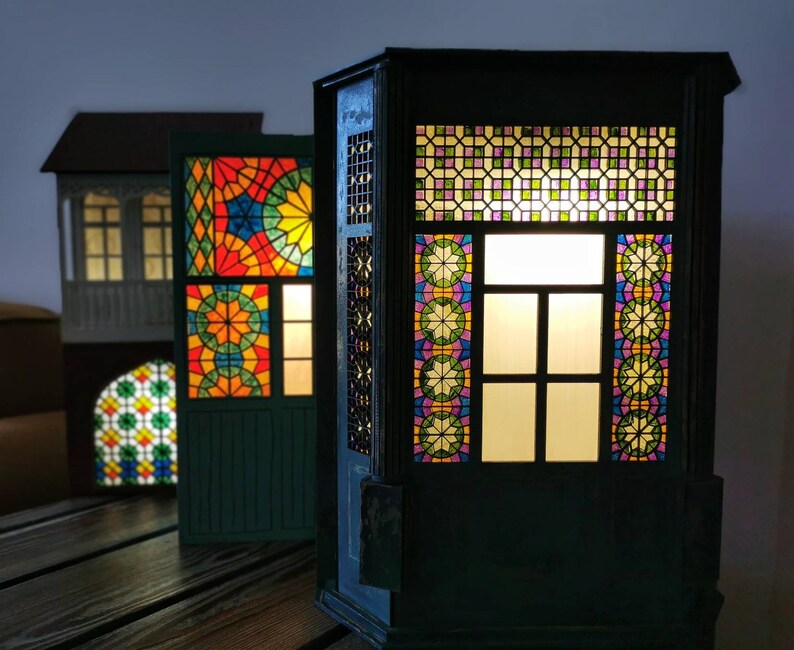 K&ouml;nnte beinhalten: Drei Miniaturgeb&auml;ude aus Holz mit Buntglasfenstern. Das Geb&auml;ude rechts hat ein beleuchtetes Fenster mit einem bunten Buntglasmuster. Das Geb&auml;ude in der Mitte hat ein buntes Buntglasmuster im Fenster. Das Geb&auml;ude links hat ein wei&szlig;es Buntglasmuster im Fenster.