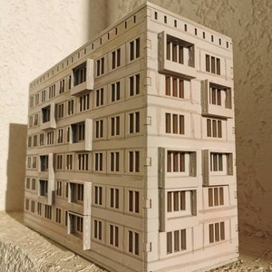 May include: A white cardboard model of a multi-story building with many windows. The model is detailed with small windows and balconies.