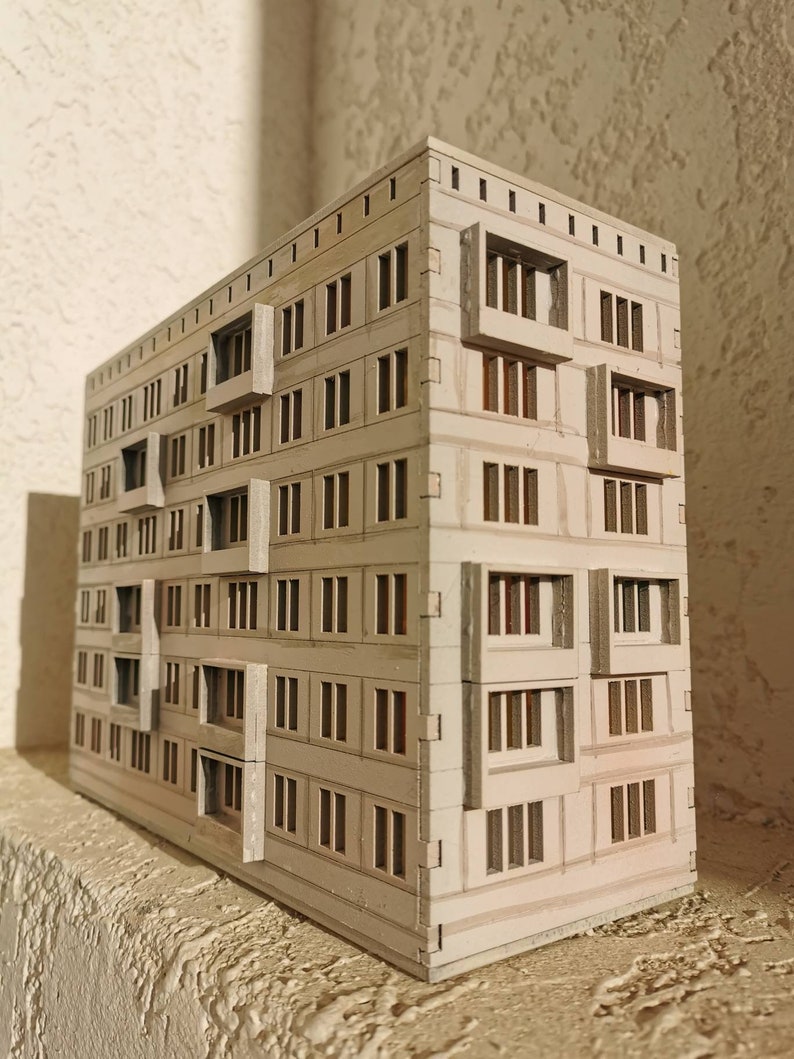 May include: A white cardboard model of a multi-story building with many windows. The model is detailed with small windows and balconies.