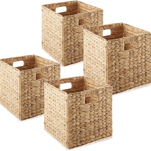 May include: Four square woven storage baskets. Each basket is a natural beige color with a square opening and built-in handles. The baskets are made of a woven material, likely natural fibers, and are designed for organizing items.
