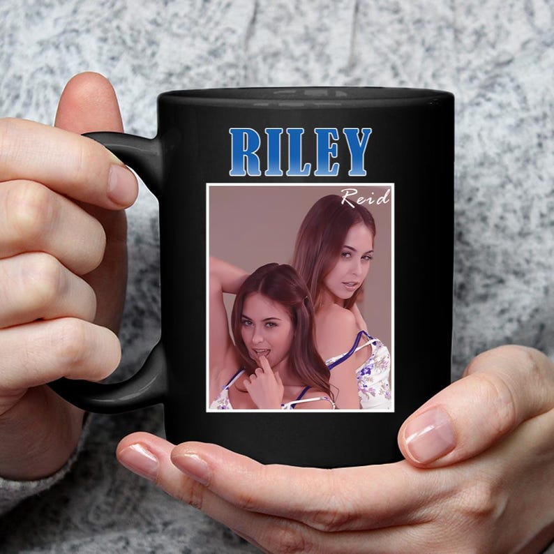 May include: Black ceramic mug featuring the name "RILEY" in blue lettering. The mug displays a framed image of two women. The name "Reid" is above the image. The mug is held by a person.