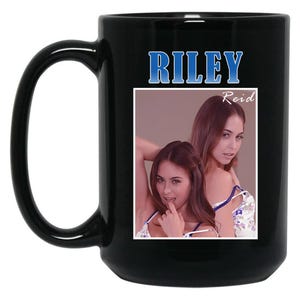 May include: Black ceramic mug with a large handle. The mug features the name "RILEY" in blue block letters above a photo of a woman. The name "Reid" is printed in white script below the name "RILEY".