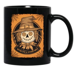 May include: A black ceramic mug featuring a graphic of a scarecrow wearing a brown hat, with button eyes and a stitched smile. The design is set against an orange background with spiderweb corners and the text "BUTTON EYES & STITCHED SMILES".