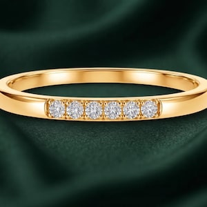 Könnte beinhalten: Ein polierter Gelbgoldring mit einer Kanalfassung, in der sechs kleine, runde, klare und facettierte Steine in einer horizontalen Reihe auf der Vorderseite des Rings angeordnet sind, mit einer glatten, reflektierenden Metalloberfläche.