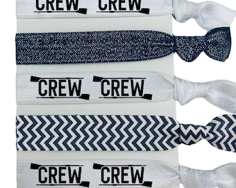 May include: A set of five hair tie elastics in various designs. Two white elastics with the word "CREW" in black, a navy blue glitter elastic, a white and navy blue chevron patterned elastic, and a white elastic with a silver bow.