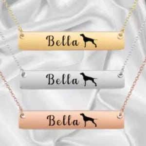May include: Three gold, silver, and rose gold bar necklaces with the name "Bella" and a silhouette of a dog engraved on each.