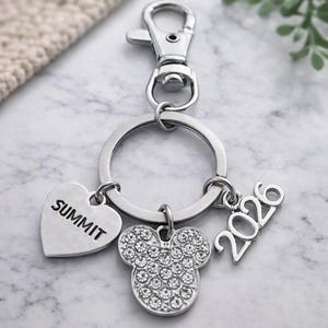 May include: Silver keychain with a heart charm that reads "SUMMIT", a Mickey Mouse head charm encrusted with rhinestones, and a "2026" charm. The keychain has a clasp and a large ring for keys.