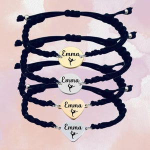 May include: Four black string bracelets with a silver and gold charm. The charms are round and heart-shaped and feature the name "Emma" and a silhouette of a gymnast.