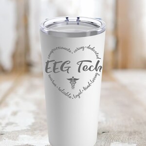 Könnte beinhalten: Ein weißer Edelstahlbecher mit einem grauen Kreisdesign, auf dem "EEG Tech" mit einem Caduceus-Symbol in der Mitte steht. Der Kreis ist umgeben von den Worten "mitfühlend, fürsorglich, engagiert, warm, zuverlässig, loyal, freundlich, liebevoll".