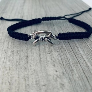 May include: Black braided bracelet with a silver charm of a tied martial arts belt.