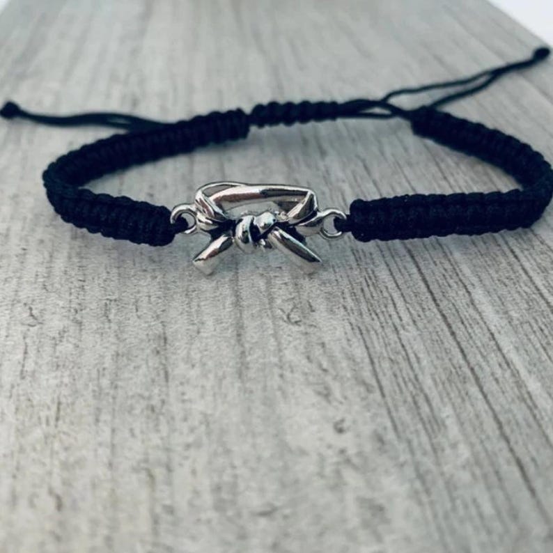 May include: Black braided bracelet with a silver charm of a tied martial arts belt.