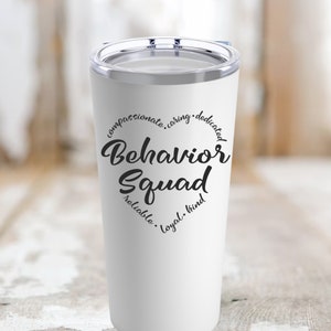 May include: A white tumbler with a clear lid. The tumbler features the words "Behavior Squad" in a heart shape, surrounded by words like "compassionate" and "caring" in black script.