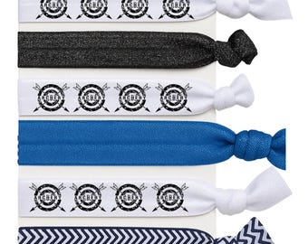 May include: A collection of hair ties in various colors and patterns. Some ties are white with a black archery target design and the word "ARCHERY". Other ties are solid black, blue, and navy with a white chevron pattern.