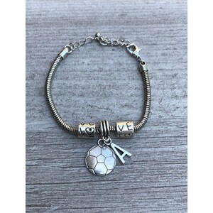 May include: A silver bracelet with a football charm and letter 'A' charm. The bracelet also has two charms that say 'LOVE' with a heart symbol.
