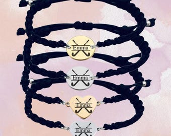 May include: Four black cord bracelets with personalized charms. The charms are silver and gold and feature the name "Emma" and a pair of crossed hockey sticks.