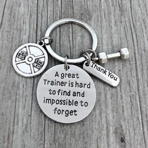 May include: Silver keyring with a weight plate charm, a dumbbell charm, and a tag that reads "A great Trainer is hard to find and impossible to forget". The tag also has "Thank You" written on the back.