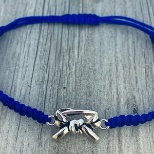 May include: A blue braided bracelet with a silver belt buckle charm.