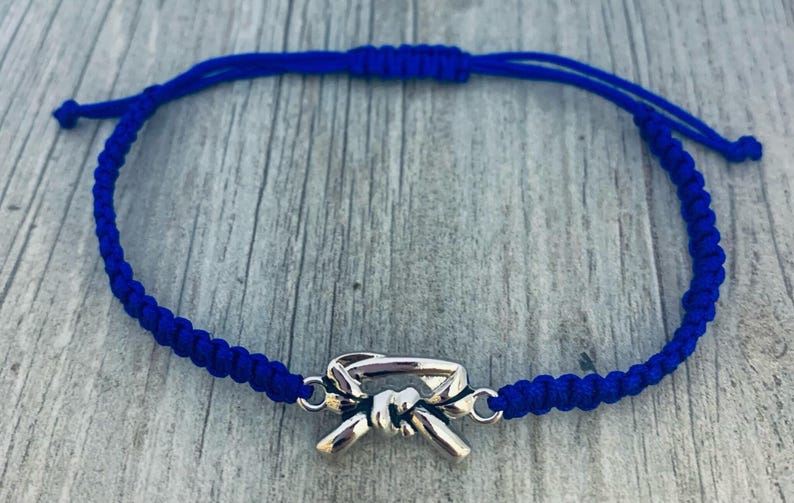 May include: A blue braided bracelet with a silver belt buckle charm.
