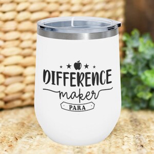 Peut inclure: Un gobelet à vin en acier inoxydable blanc avec un motif noir de pomme et d'étoiles et le texte "Difference maker PARA".
