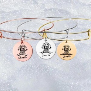 May include: Three expandable bangle bracelets with a round charm featuring a dog's head and the name "Charlie" engraved on each charm. The bracelets are available in rose gold, silver, and gold.