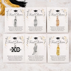 May include: Six graduation tassel charms on cards. Each card has the text "Tassel Charms" and a quote. The charms include a running shoe, a cross country shoe, a winged shoe, and an XC symbol. Gold and black tassels are in the background.