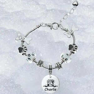 May include: Silver charm bracelet with a dog paw print charm, bone charms, and a round charm with a dog's face and the name "Charlie" engraved on it.