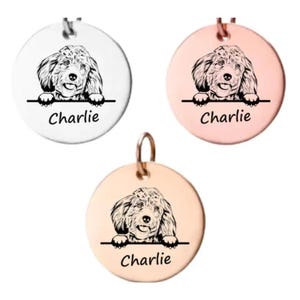 May include: Three round silver, rose gold, and gold pendants with a black and white illustration of a dog peeking over the top. The pendants have the name "Charlie" engraved on the bottom.
